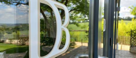 A large white letter 'B' on a glass door, with a view of a wooden deck and greenery outside.
