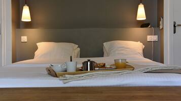 A neatly made bed with a tray of breakfast items including a cup, a pot, and a glass of juice.