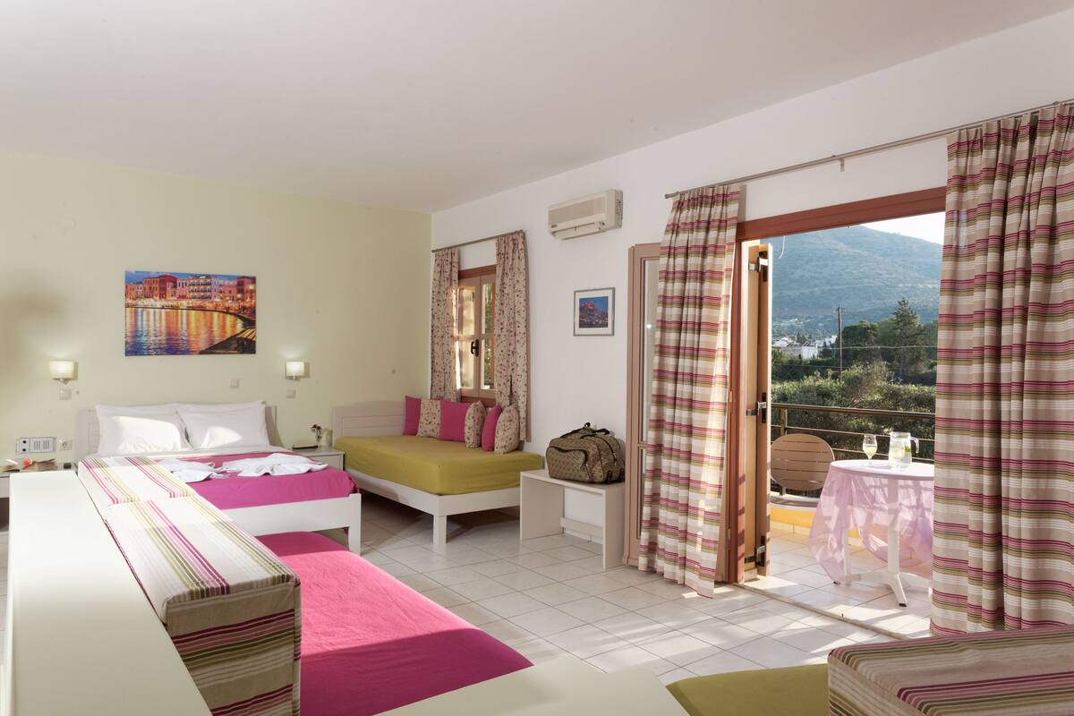 A hotel room with a bed, a sofa, a small table with a pitcher, and a view of the outdoors.