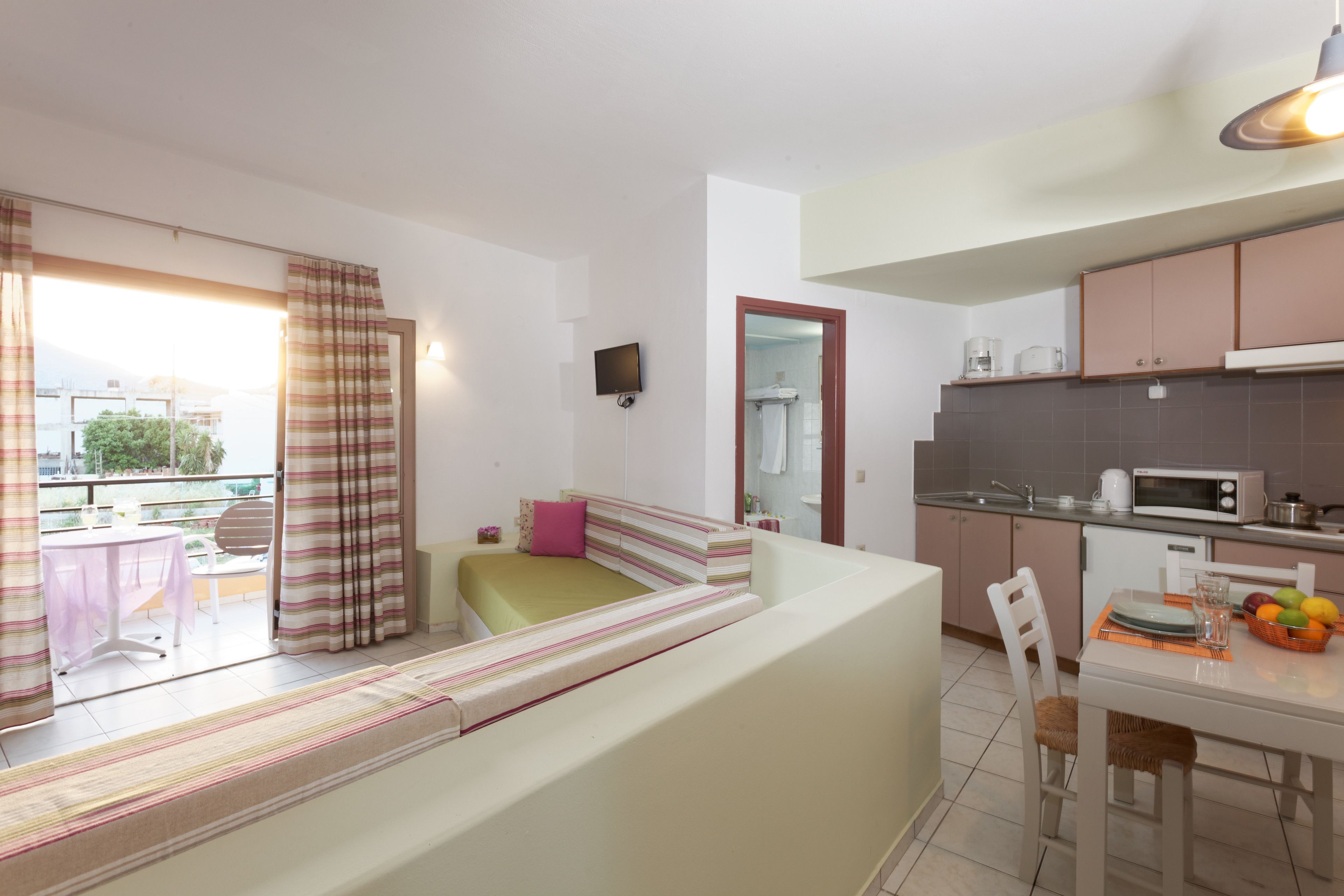 Un appartamento moderno con balcone, angolo cottura, zona pranzo e soggiorno con divano e televisione.
