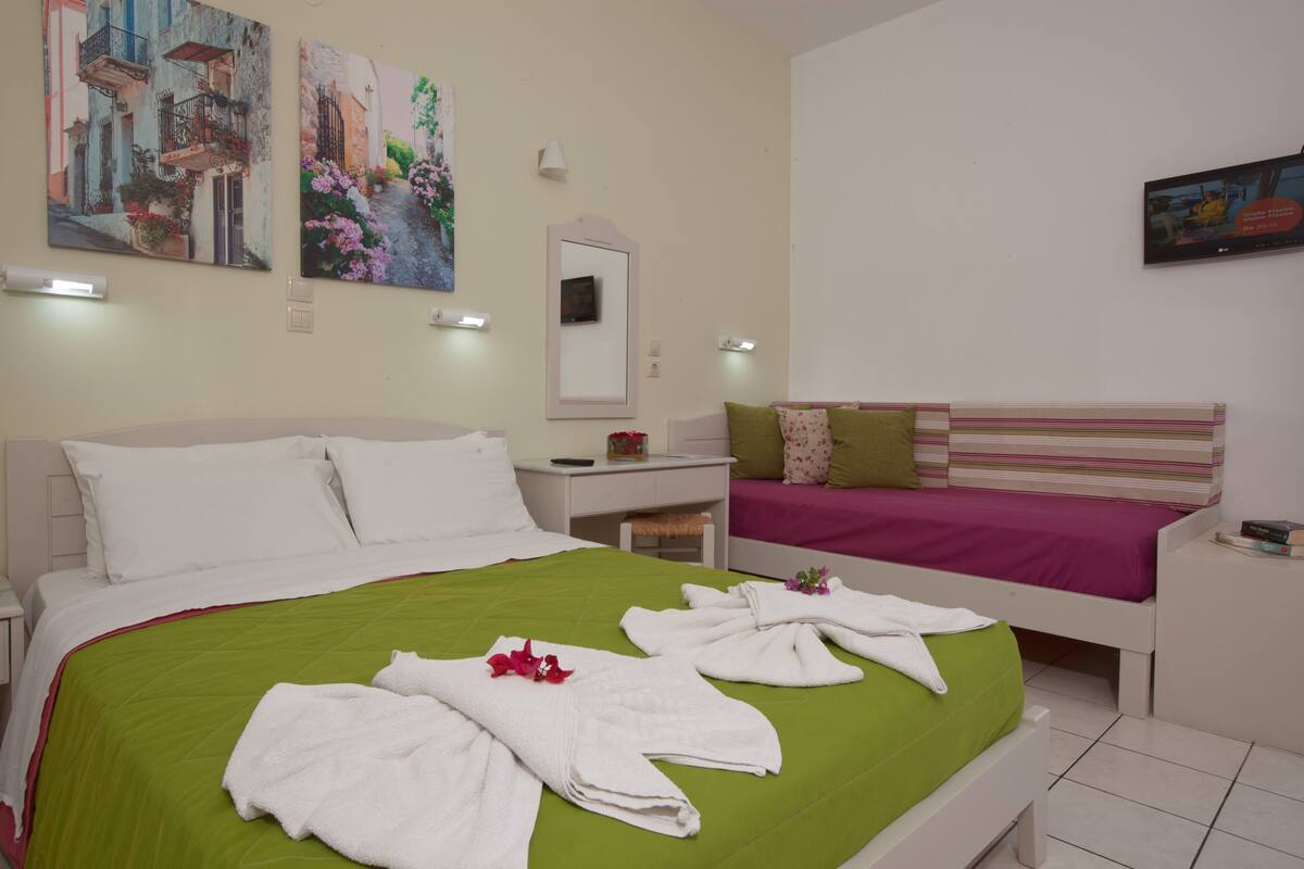 A hotel room with a green bedspread, white pillows, a striped headboard, and artwork on the walls.