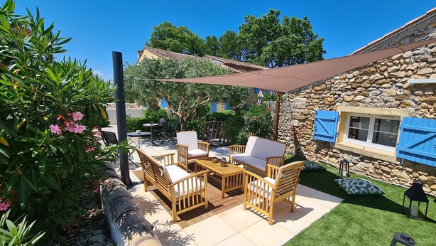 An outdoor patio with wooden furniture, a stone wall, and a blue shuttered window. - Logis Hotel La Bastide St Bach (Suze-la-Rousse)