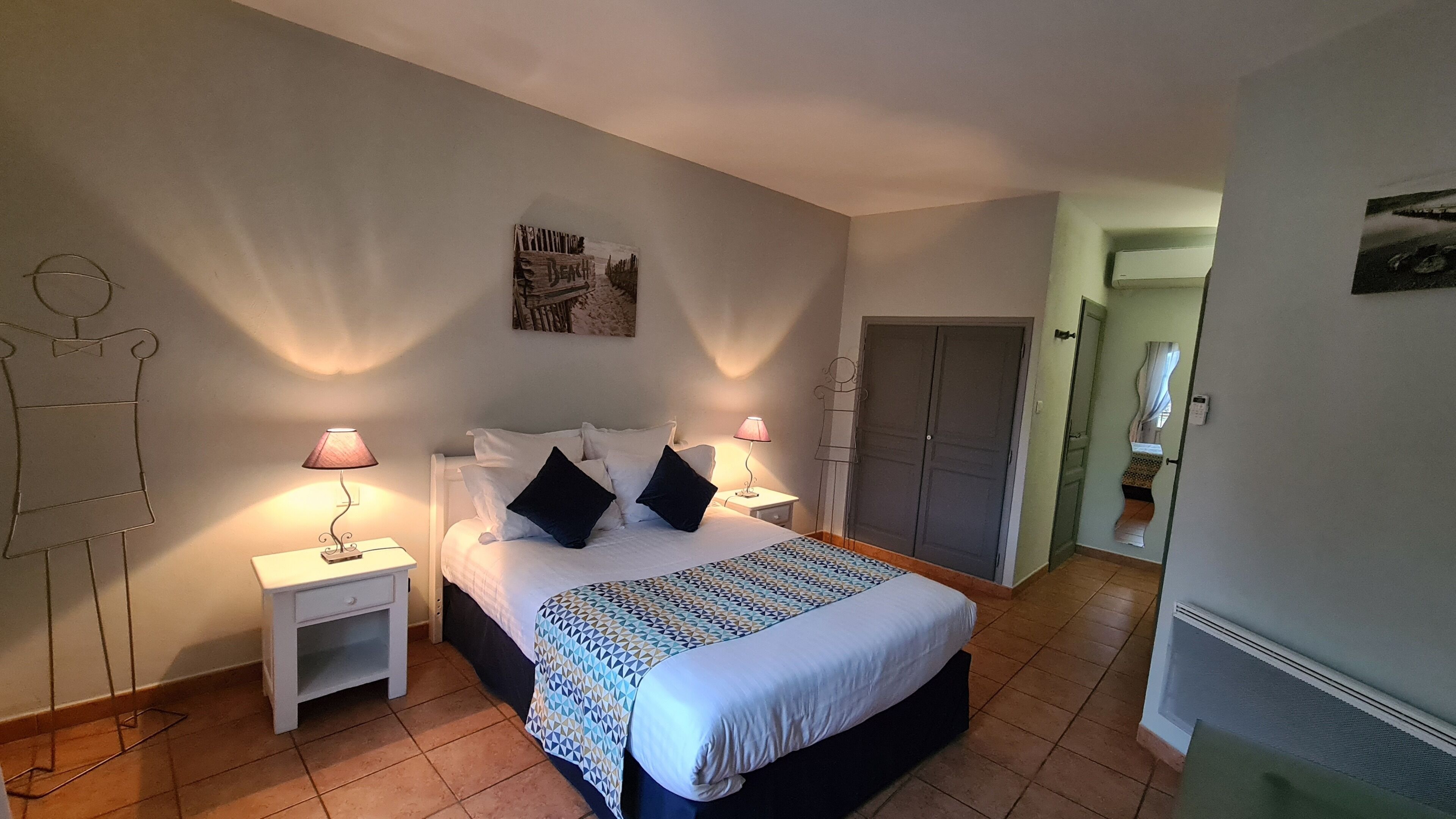 Quarto com cama, duas mesas de cabeceira com luminárias, guarda-roupa e um cartaz na parede.