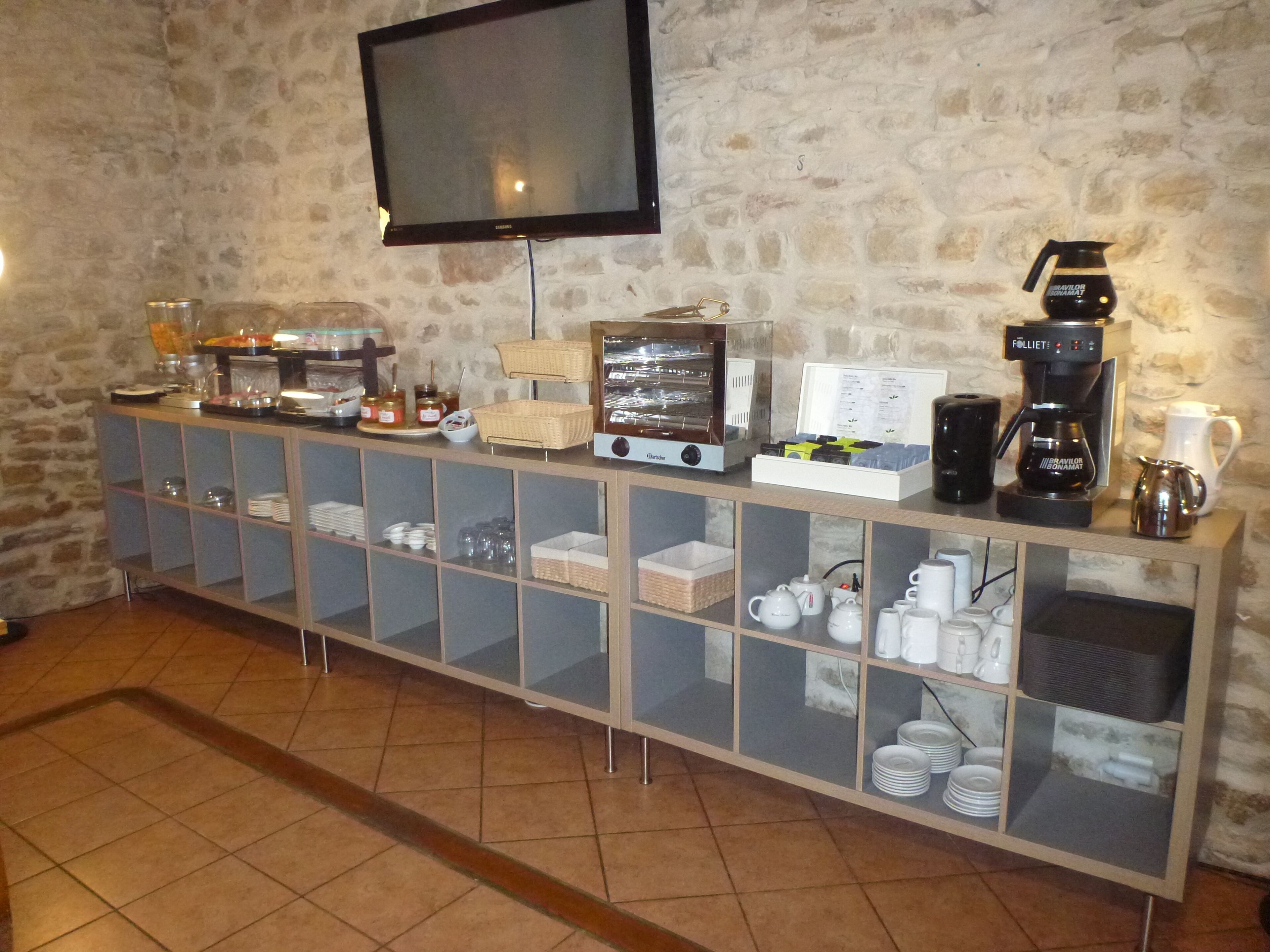 Ein Frühstücksbuffet mit Flachbildfernseher, Kaffeeautomaten und einer Auswahl an Speisen.