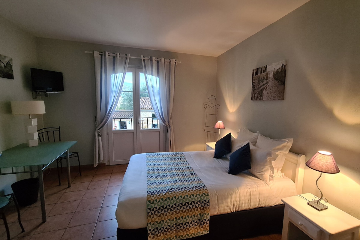 Un dormitorio con cama, mesita de noche, lámpara, ventana con cortinas, escritorio, silla y televisor.