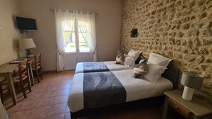A bedroom with two beds, a desk, a chair, a TV, and a stone wall. - Logis Hotel La Bastide St Bach (Suze-la-Rousse)