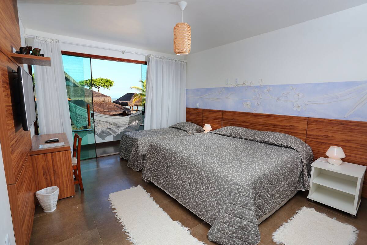 Un dormitorio con cama, mesitas de noche, televisor y vistas al exterior.