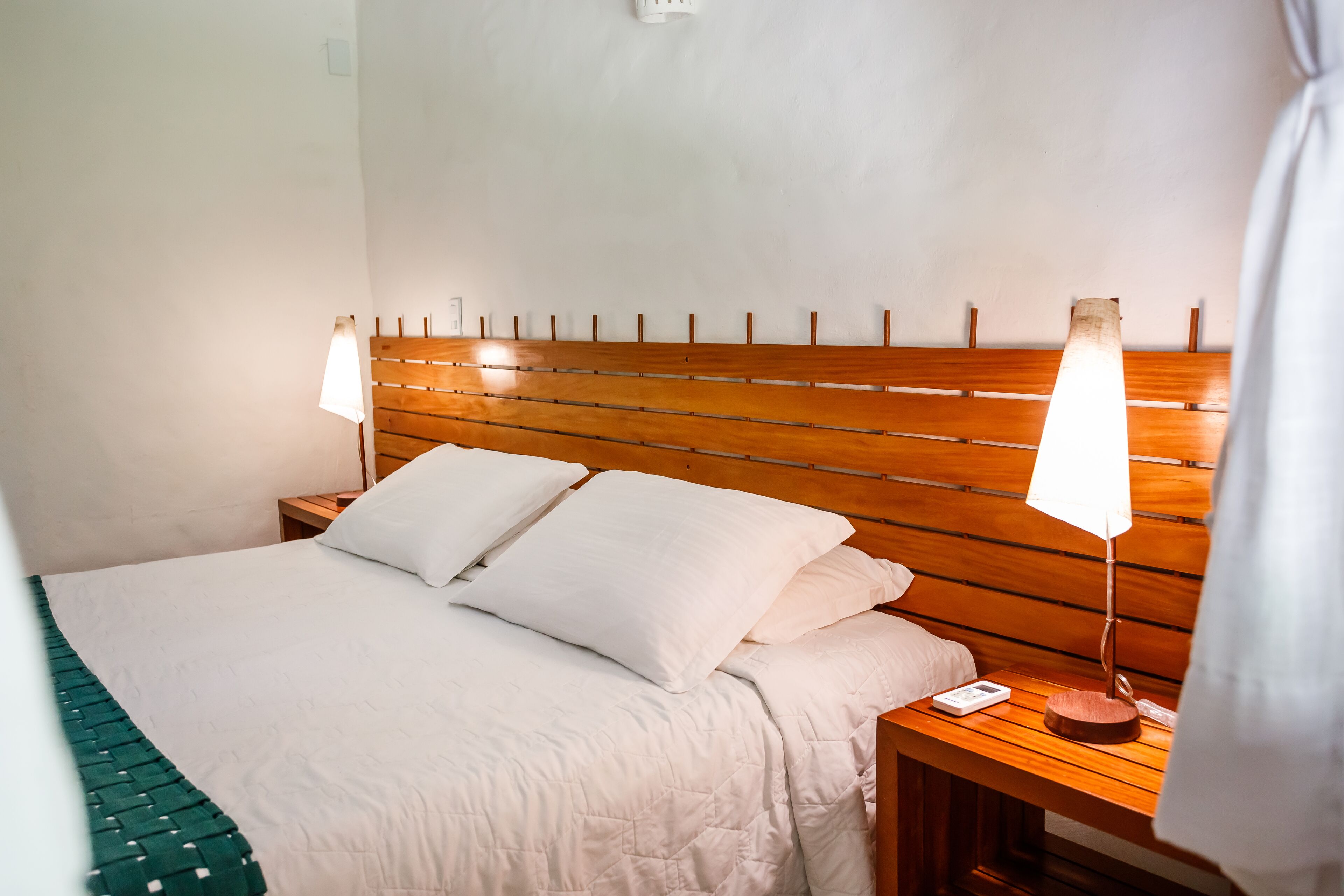 A neatly made bed with a wooden headboard, two bedside lamps, and a bedside table with a lamp and a phone.