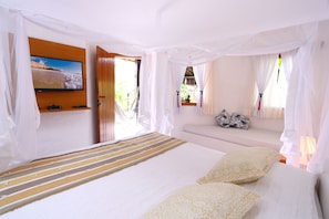 Un dormitorio con cama, televisor montado en la pared y ventana con cortinas.