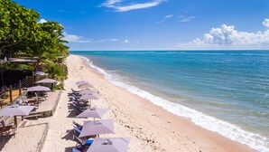 A beach with rows of sun loungers and umbrellas, a wooden fence, and a view of the ocean. - Pousada Rigatoni Beach (Porto Seguro)