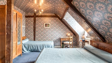 Un dormitorio acogedor en el ático, con dos camas, vigas de madera y papel tapiz estampado.