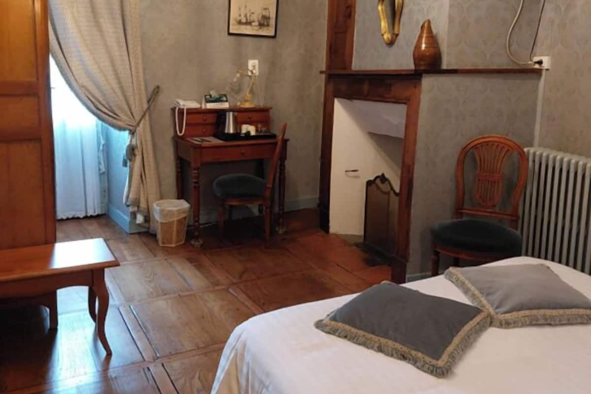 Een slaapkamer met een houten bed, een bureau, een stoel, een radiator en een televisie aan de muur.