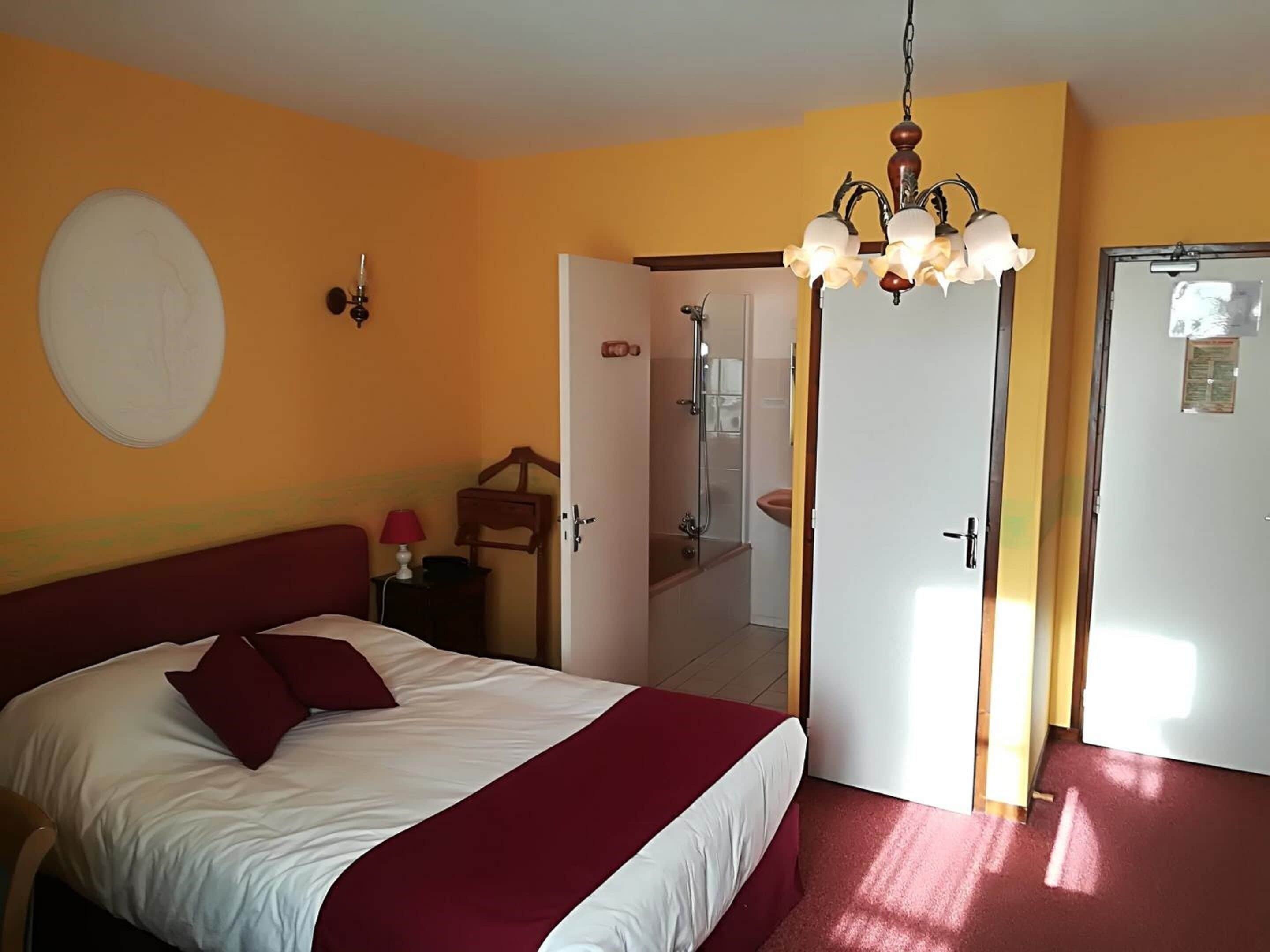 Une chambre à coucher comprenant un lit, une table de chevet, une lampe, une horloge murale, une porte donnant sur une salle de bain et un lustre.
