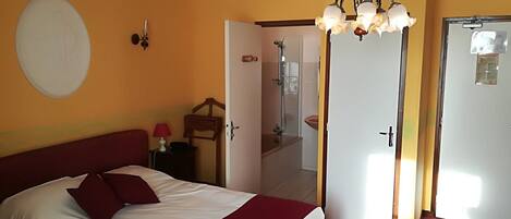 Une chambre à coucher comprenant un lit, une table de chevet, une lampe, une horloge murale, une porte donnant sur une salle de bain et un lustre.
