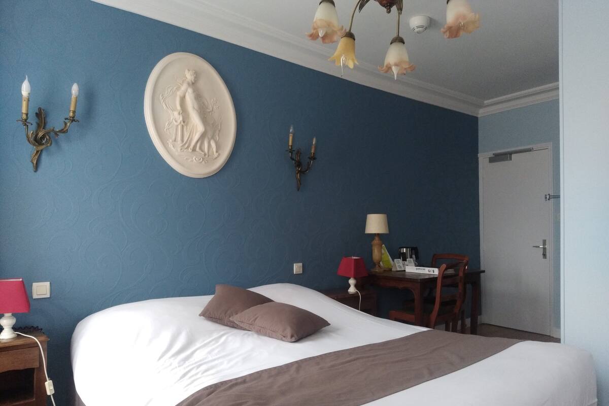 A hotel room with a large bed, a nightstand with a lamp, a wall-mounted candelabra, and a decorative plate.
