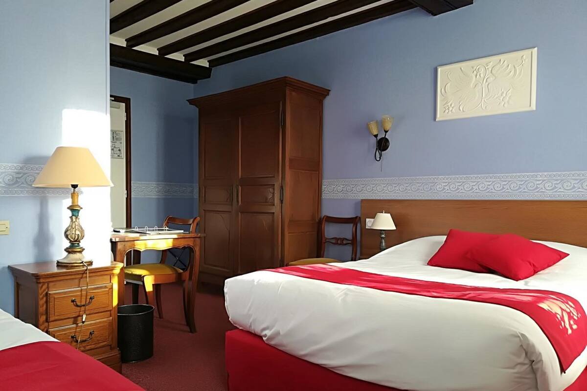 A hotel room with two beds, a wooden wardrobe, a desk, and a chair.