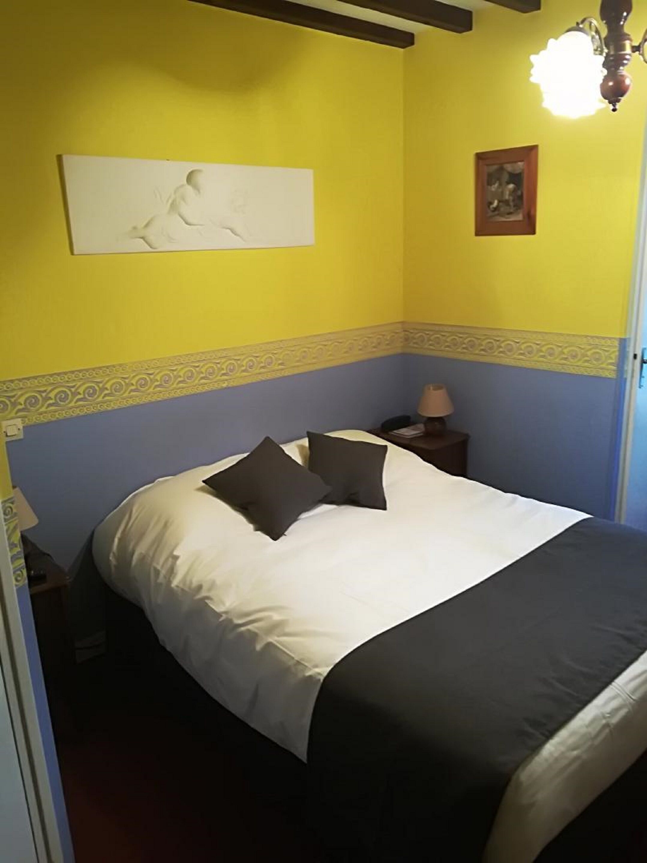 A bedroom with a bed, pillows, a nightstand, a lamp, and a wall decoration.