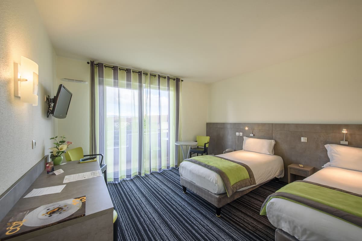 A hotel room with two beds, a desk, a chair, a small table, and a window with curtains.