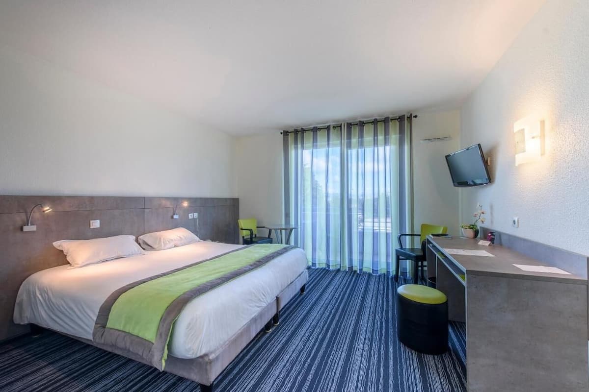 A hotel room with a bed, a desk, a chair, a TV, and a window with curtains.