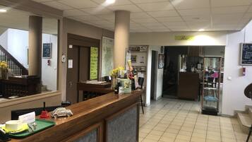 Un espace d’accueil comprenant un comptoir en bois, un petit bureau et un coin salon avec une chaise.