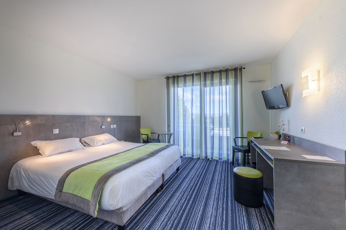 A hotel room with a bed, a desk, a chair, a TV, and a window with curtains.