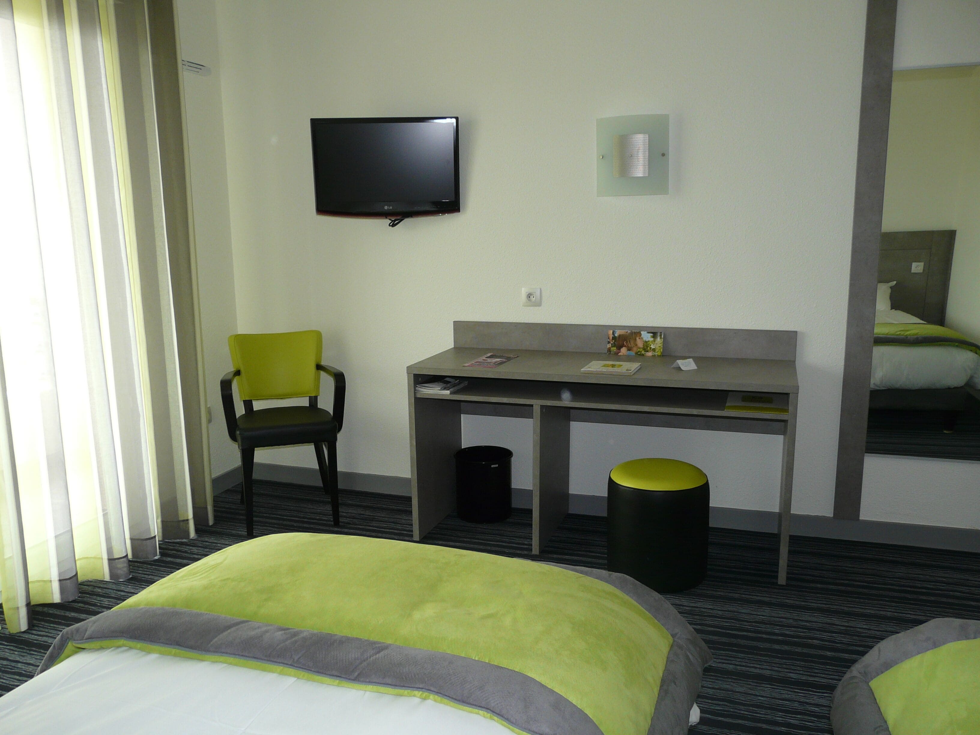 A hotel room with a bed, a desk, a chair, a television, and a trash can.