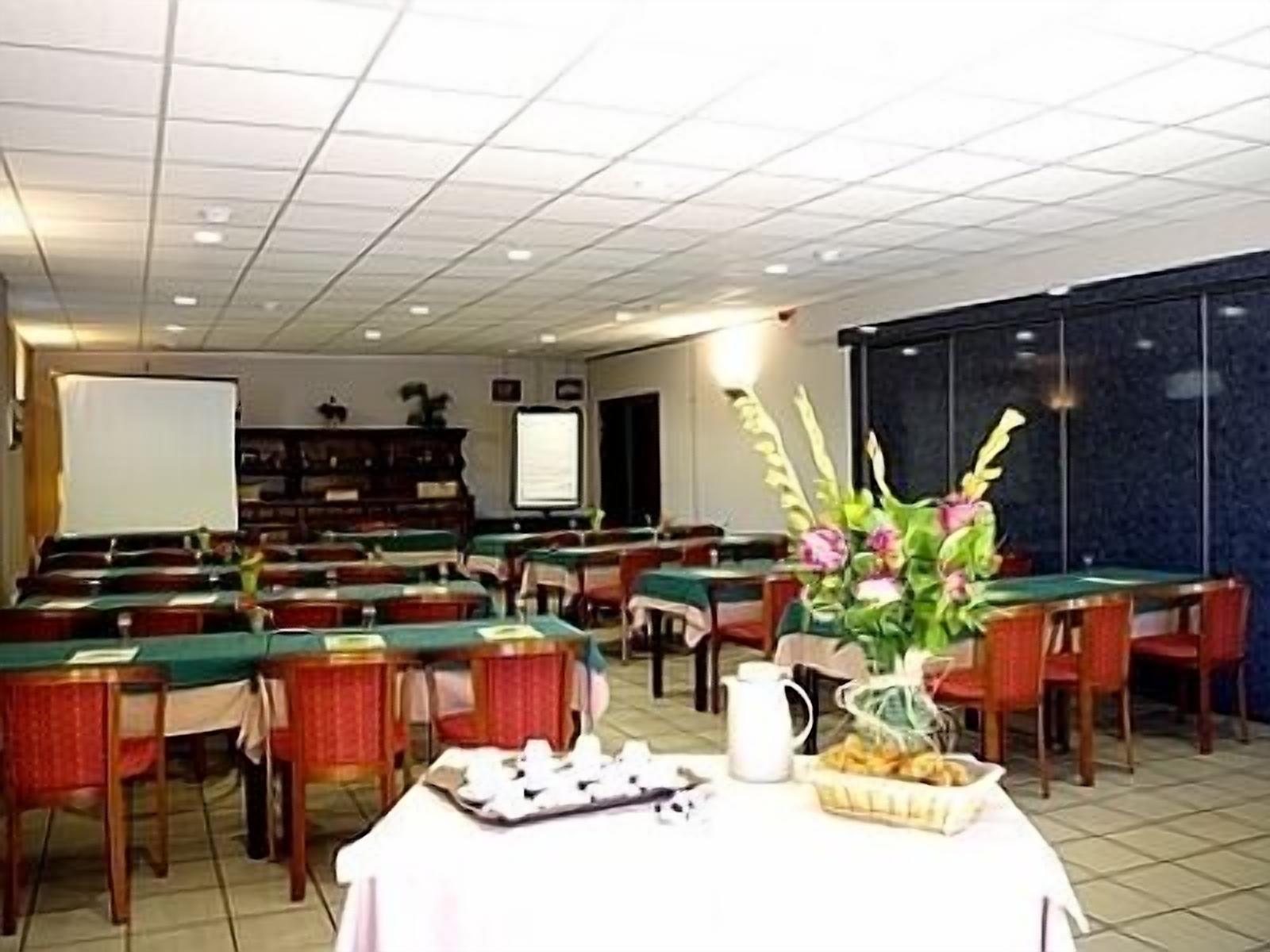 Un salón de conferencias con varias mesas, sillas, una pantalla de proyector y un arreglo floral.