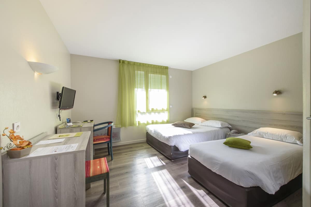 A hotel room with two beds, a desk with a chair, a TV, and a window with green curtains.