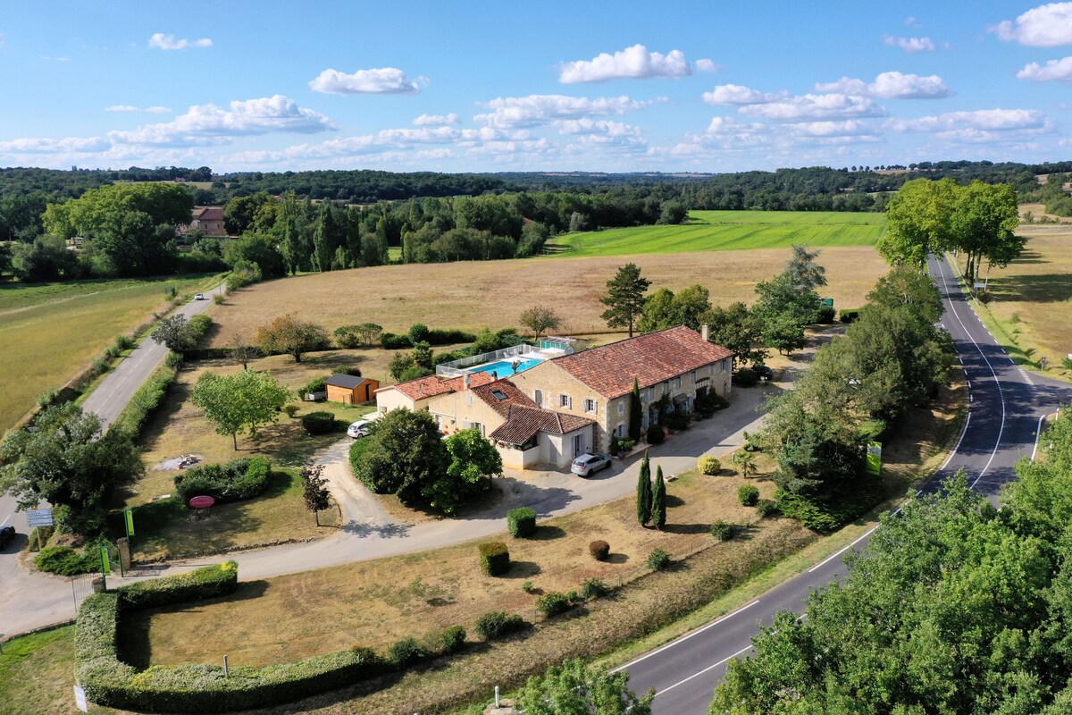A large house with a swimming pool, surrounded by green fields and a curved road.