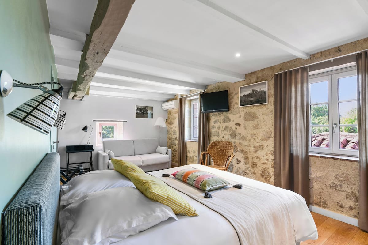 A bedroom with a bed, a chair, a desk, and a TV.