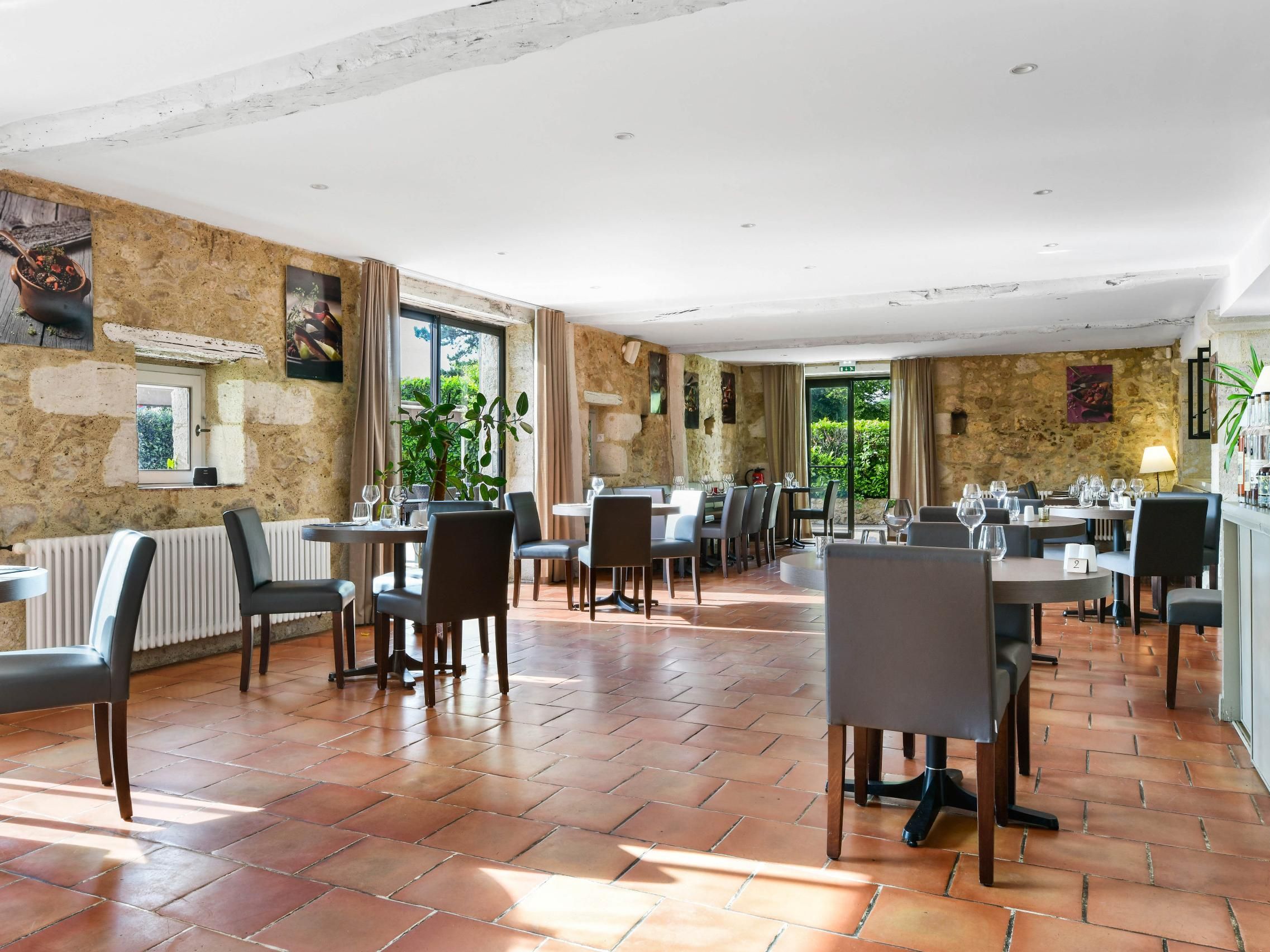A spacious dining area with multiple tables and chairs, stone walls, and large windows allowing natural light.