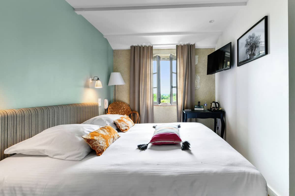 A hotel room with a bed, a chair, a desk, a lamp, and a window with curtains.