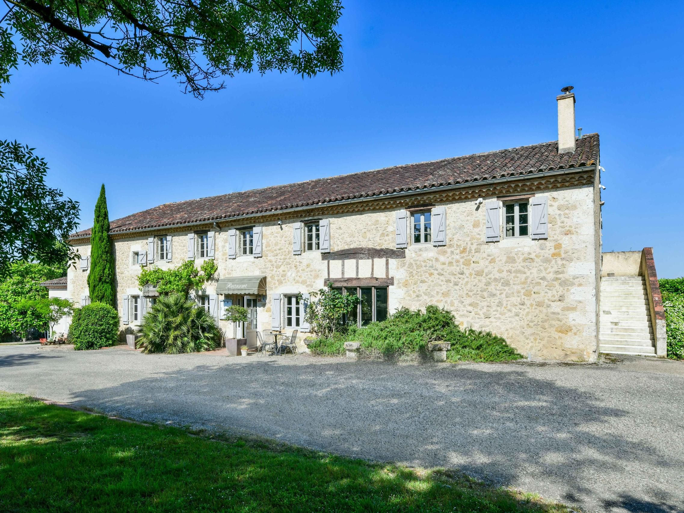 Un bâtiment en pierre avec un toit recouvert de tuiles, de nombreuses fenêtres dotées de volets et une entrée centrale.