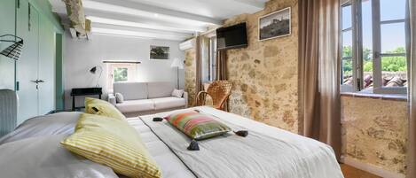 A bedroom with a large bed, a sofa, a TV, and a window with curtains.