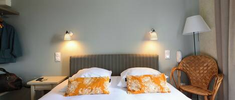 A hotel room with a bed, two bedside lamps, a chair, a nightstand, and a coat rack.