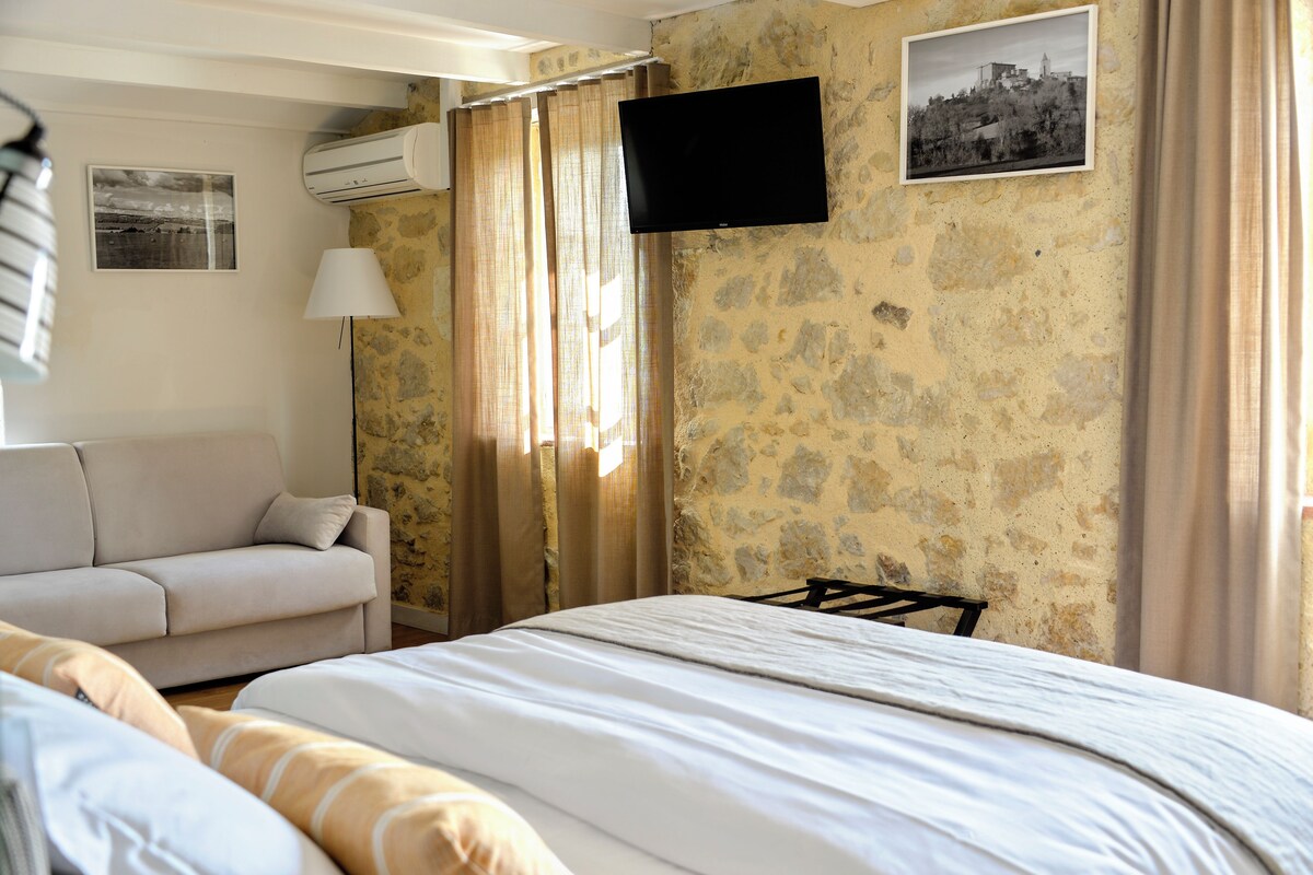 A hotel room with a bed, a sofa, a TV, and a window with curtains.