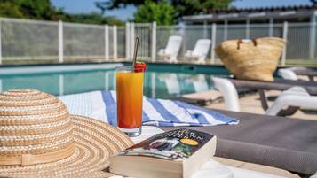 En avkopplande miljö vid poolen med en halmhatt, en bok och ett glas apelsinjuice.