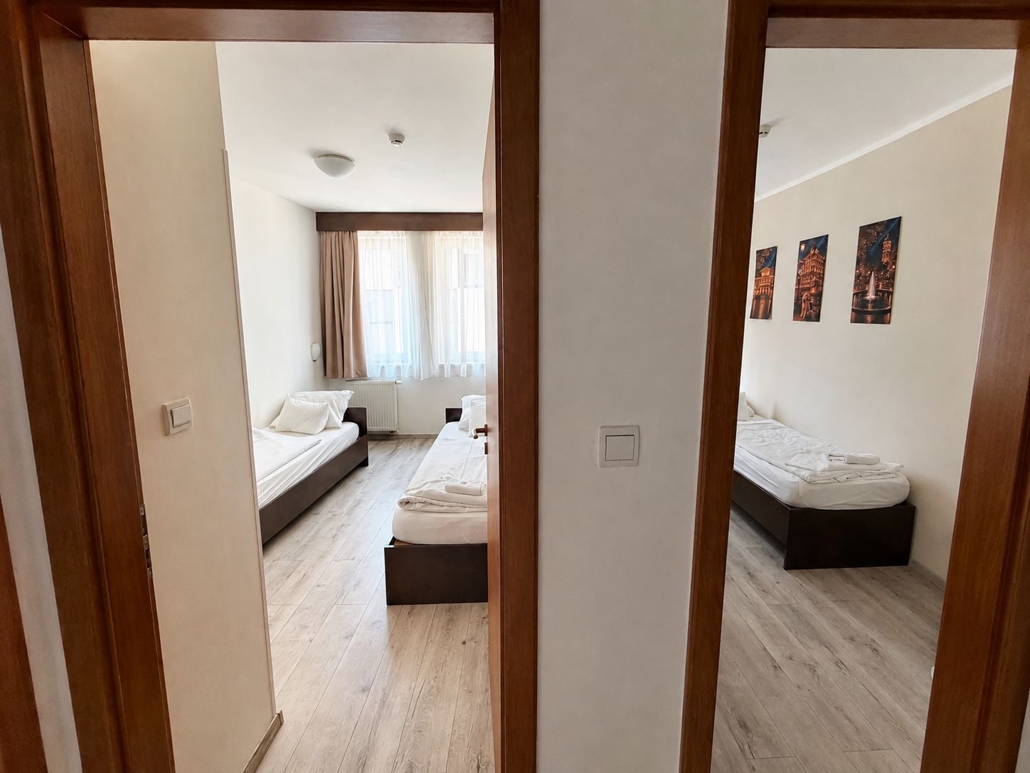Une chambre d’hôtel avec deux lits, une fenêtre avec des rideaux et un mur orné de tableaux.