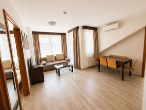 A modern living room with a sofa, coffee table, and dining table with chairs. There is a window with curtains, an air conditioning unit, and a ceiling light. - Prater Residence (Budapest)