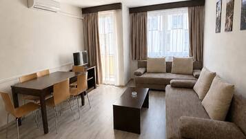 Een moderne woonkamer met een bank, een salontafel, een eettafel met stoelen en een televisie.