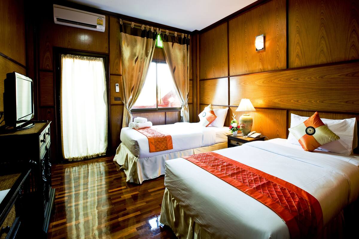Quarto de hotel com duas camas, televisão, escrivaninha e janela com cortinas.