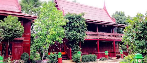 A traditional red-roofed building with a balcony, surrounded by lush greenery and potted plants.
