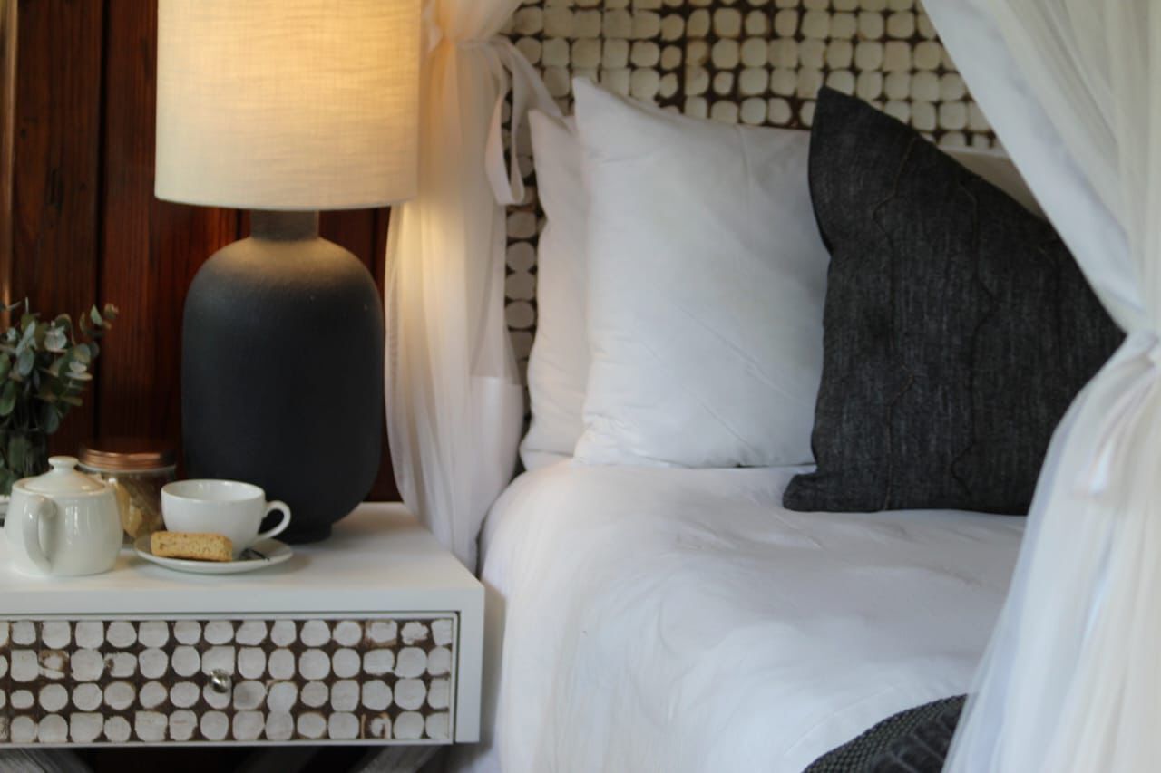 A neatly made bed with white and gray bedding, a bedside table with a lamp, a cup, and a small container.