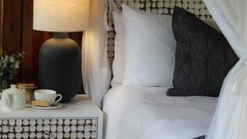 A neatly made bed with white and gray bedding, a bedside table with a lamp, a cup, and a small container.