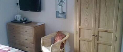 Un dormitorio con tocador de madera, una silla de mimbre, un televisor en la pared y un armario.