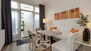 A modern living room with a dining area, featuring a sofa, chairs, a table, and artwork on the wall.