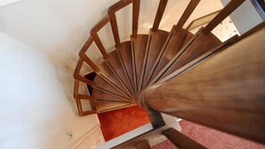 A wooden spiral staircase with a red carpet at the bottom.