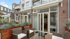 A patio area with wicker furniture, a glass table, and a brick wall. - Hotel Bor Scheveningen (The Hague)