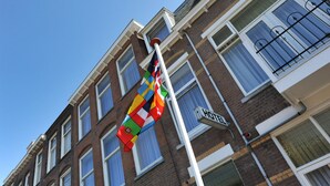 A flagpole with a flag, a sign reading "HOTEL", and a brick building with multiple windows and balconies. - Hotel Bor Scheveningen (The Hague)