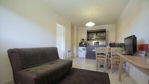 Un espace de vie compact comprenant un canapé, une table à manger avec des chaises, un coin cuisine et un téléviseur.